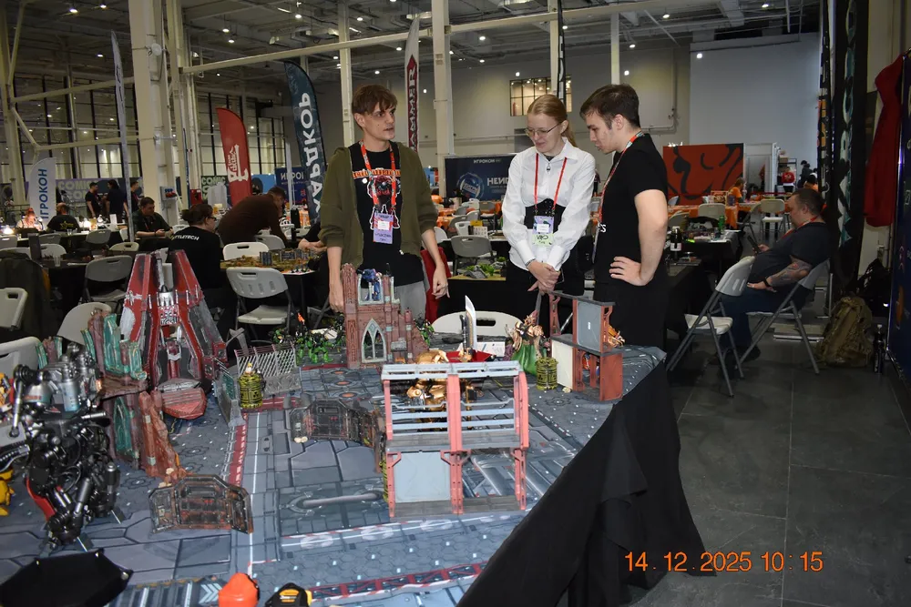 Трое человек обсуждают стол с миниатюрной моделью или игрой на игровом мероприятии.