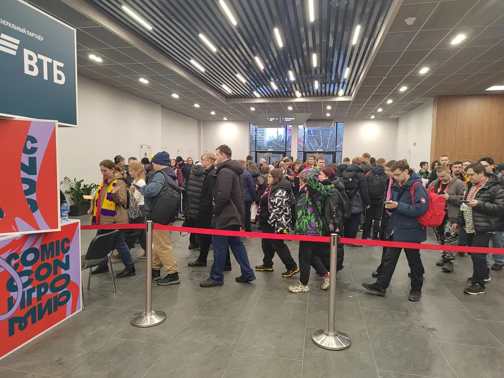 На картинке изображена очередь людей в помещении. Видно вывеску с надписью \