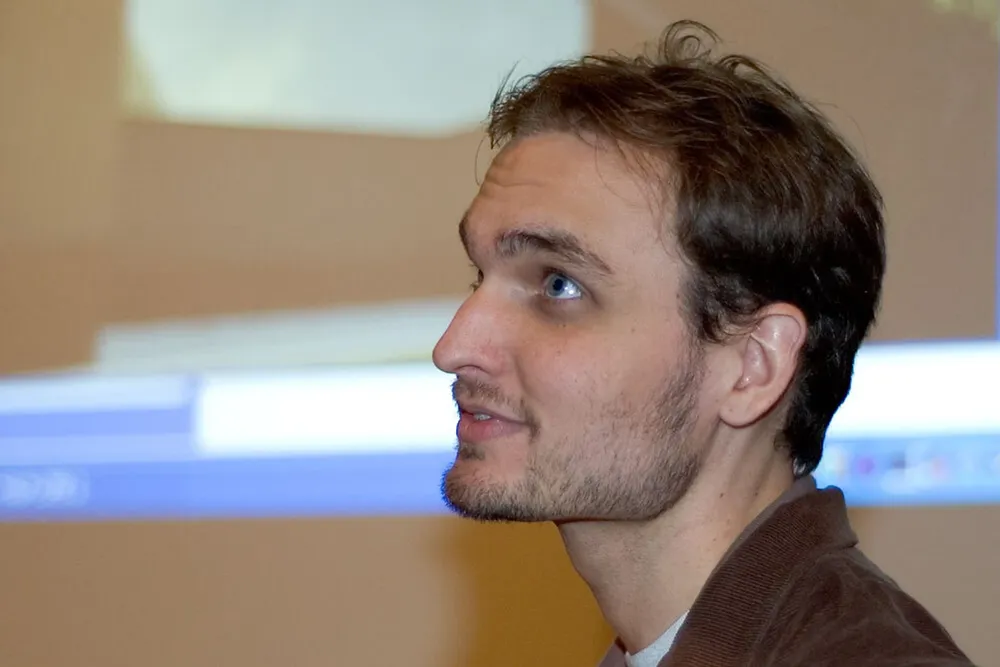 Портрет мужчины, на заднем плане размытое изображение экрана.