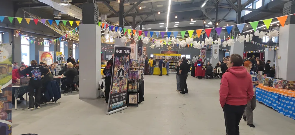 Изображение интерьера торгового помещения, люди, стоящие и сидящие за столами, выставочные стенды, праздничные украшения.