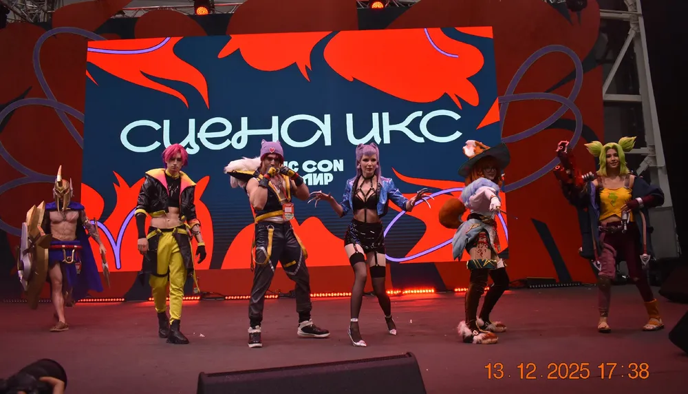 Группа людей в костюмах на сцене, выступление, яркое освещение и фон с надписью.