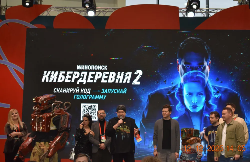 Изображение с людьми на мероприятии, фоновый экран с текстом "КИБЕРДЕРЕВНА 2" и изображениями в стиле киберпанк.