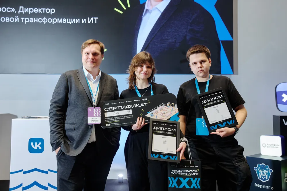 На изображении три человека, которые держат сертификаты и дипломы на фоне стенда с логотипом VK. Визуальные элементы мероприятия или награждения.