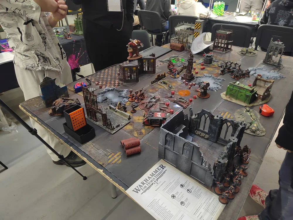 Изображение стола с миниатюрами, вероятно, для настольной игры. На столе расположены различные модели зданий и фигурки.