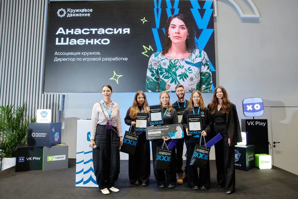 Изображение группы людей на мероприятии, с наградами и плакатом с именем.