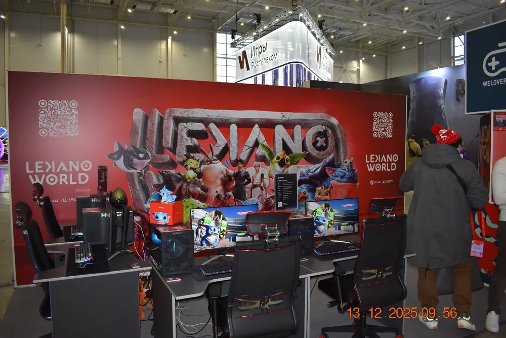 Изображение выставочного стенда с компьютерами и людьми, занимающимися игровыми активностями.