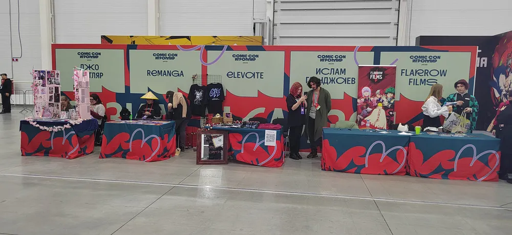 Изображение ярмарки или выставки с несколькими стендами, на которых представлены товары. Люди на переднем плане, занимающиеся различной деятельностью.