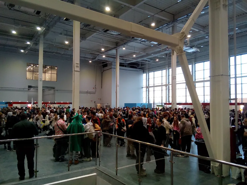 Изображение большого скопления людей в помещении, возможно, на мероприятии или выставке.