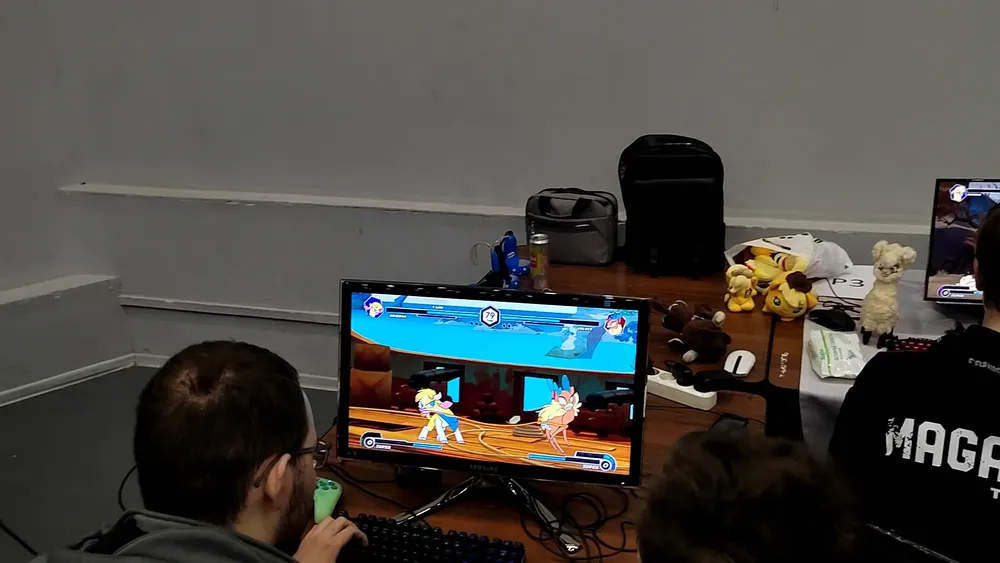 Два человека играют за компьютерами, на экране видна игровая сцена.