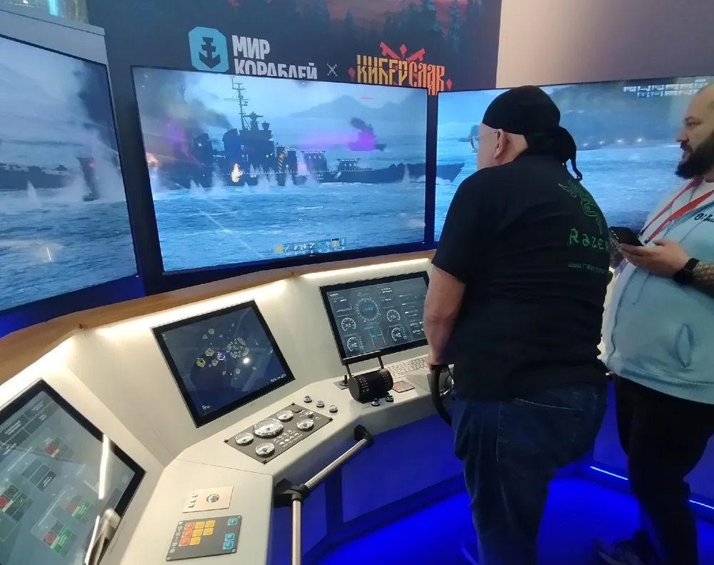 Два человека взаимодействуют с симулятором на выставке, экраны показывают военную тематику с кораблями.